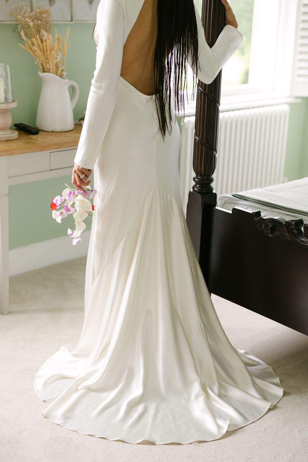 Elegant white wedding dress with open back design and long sleeves shown from behind with flowing train on carpet.