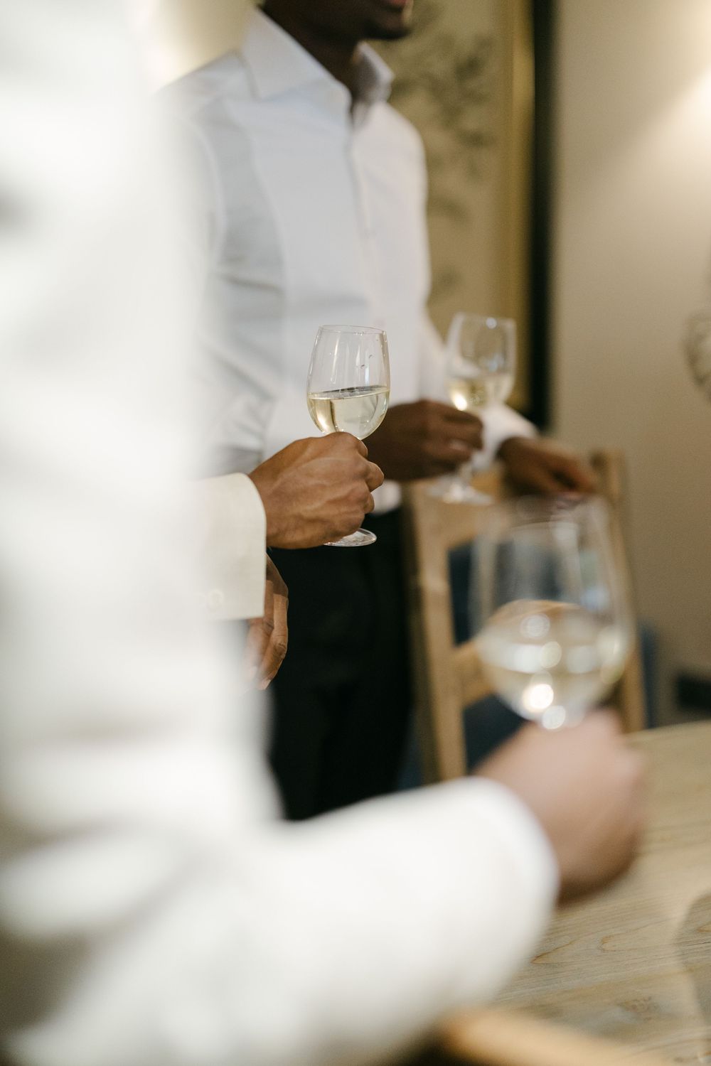 A blurred sequence of hands holding wine glasses in an elegant dining setting with white tablecloths.