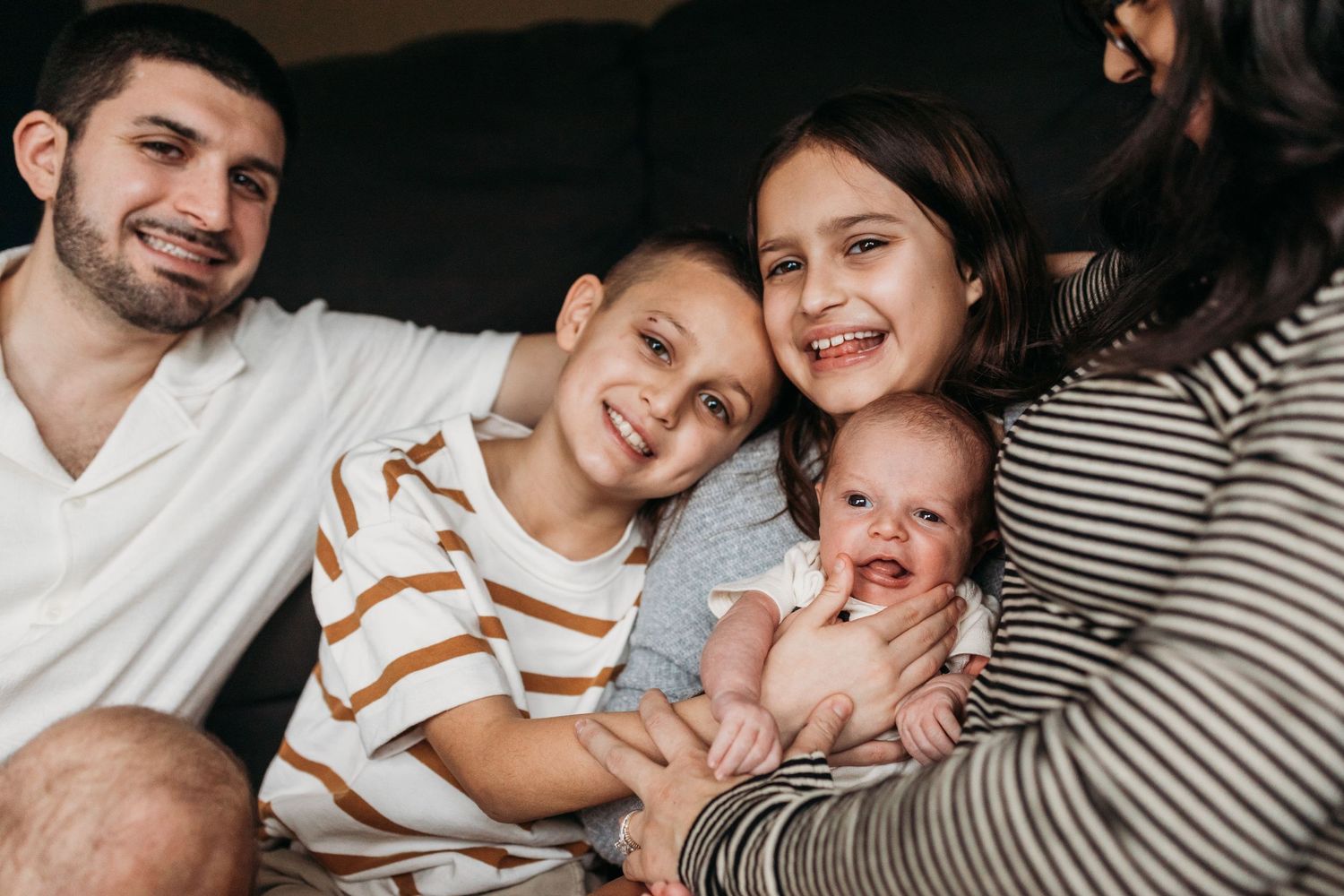 A family lounges together on a couch, sharing smiles and cuddles with their baby.