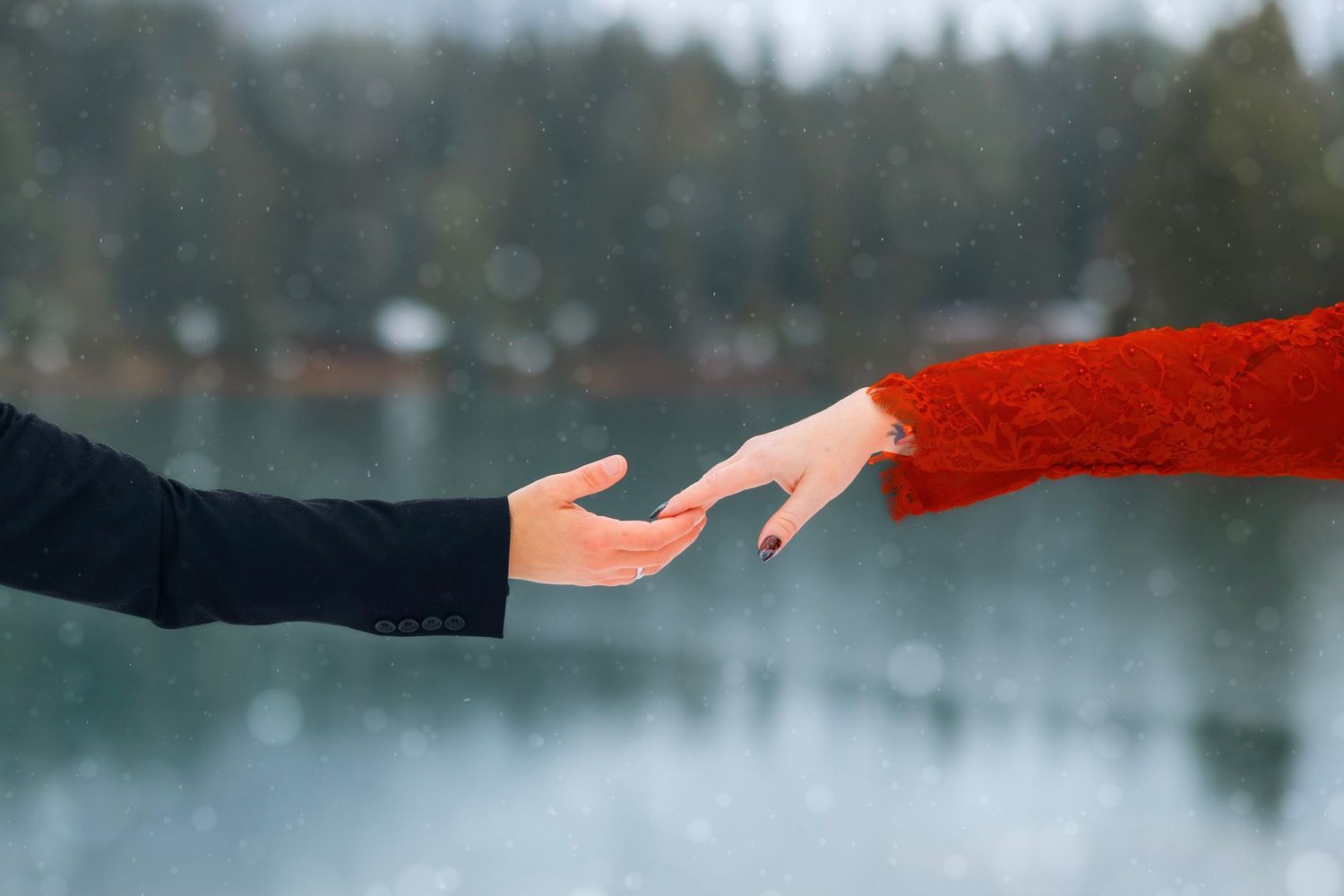 A red scarf blows in the wind against a snowy winter landscape with evergreen trees and a lake in the background.