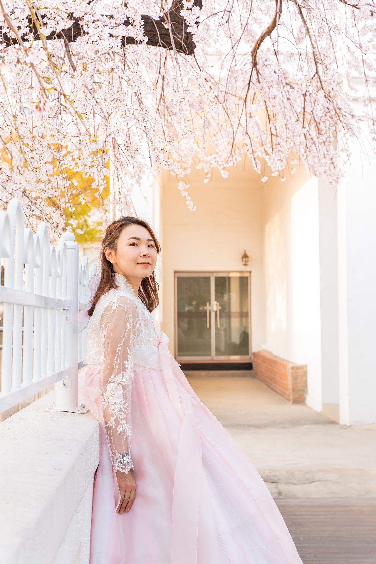 A dreamy spring scene with cherry blossoms and a flowing pink gown in an elegant white columned corridor.