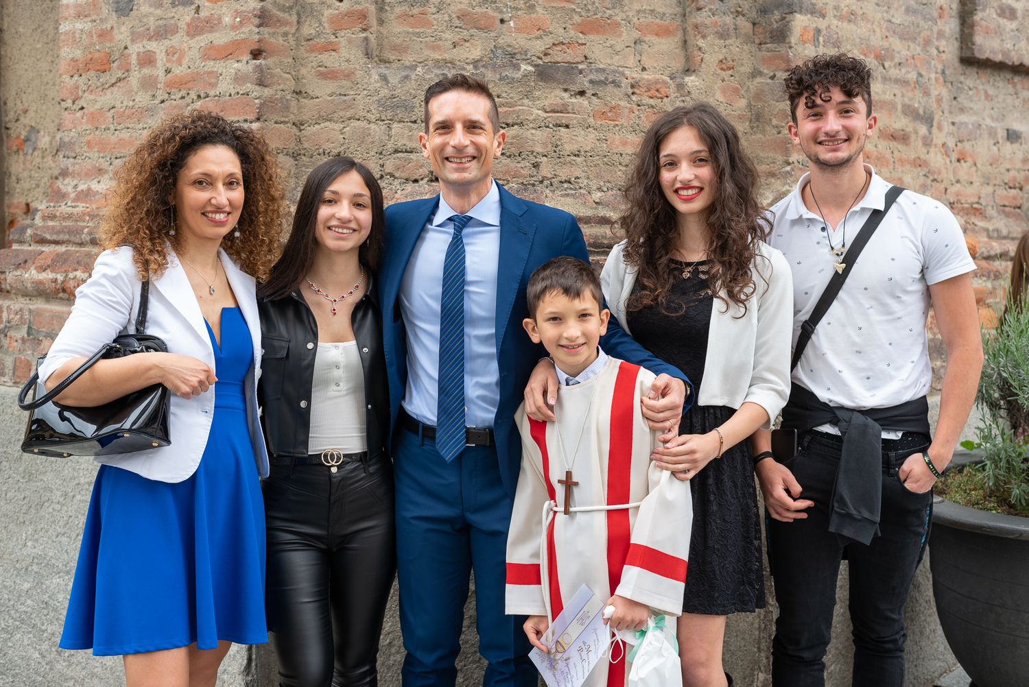 A group in formal attire poses together against a brick wall during a special occasion celebration.
