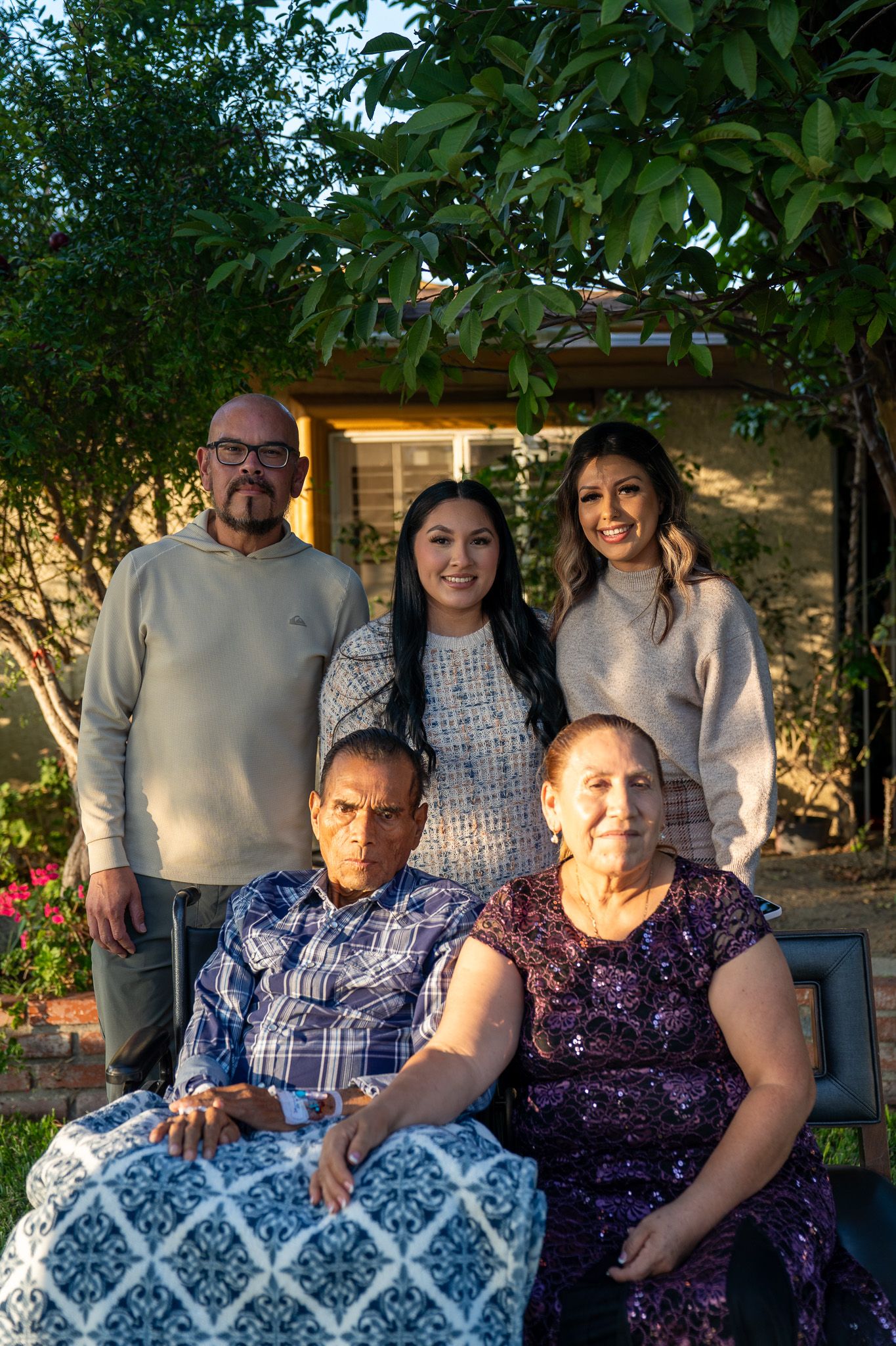 A family gathering outdoors with people sitting together on a bench in casual attire during evening light.