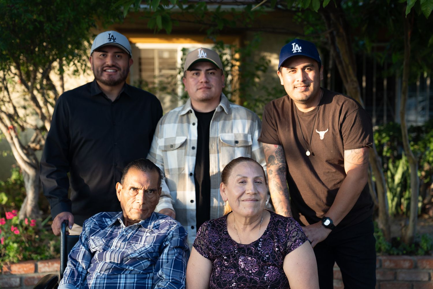 Outdoor family portrait with people wearing casual attire and baseball caps in a garden setting.