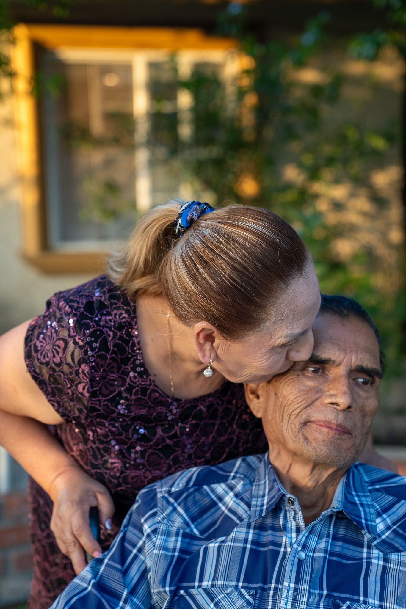 Two people sharing an intimate embrace outdoors with natural foliage in the background.