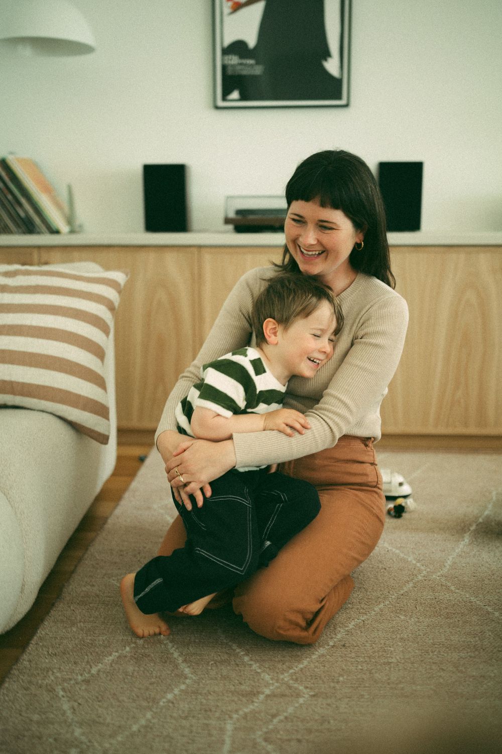 A mother and young son share a joyful hug on the floor of a modern living room.