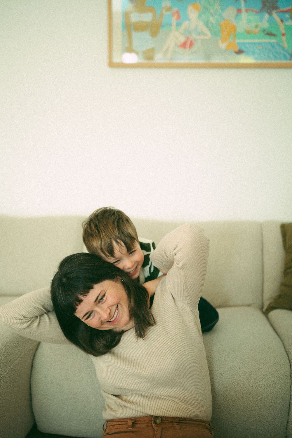 A person in a beige sweater lies comfortably on a gray couch while smiling and relaxing at home.