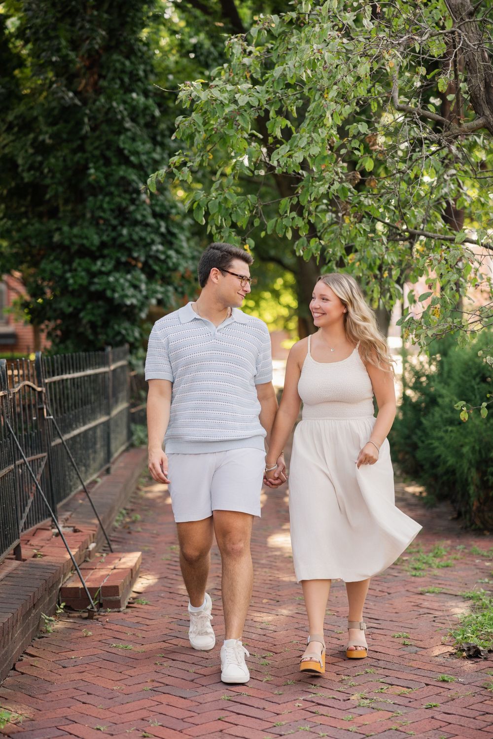 Couple walking hand in hand on a brick pathway surrounded by lush green foliage on a sunny summer day. German Village Columbus Ohio