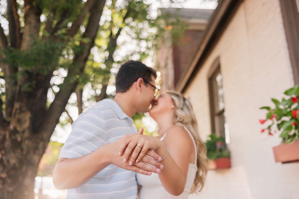 Intimate couple embracing near a white stucco wall with trees and window boxes in the background. German Village Columbus Ohio Engagement.