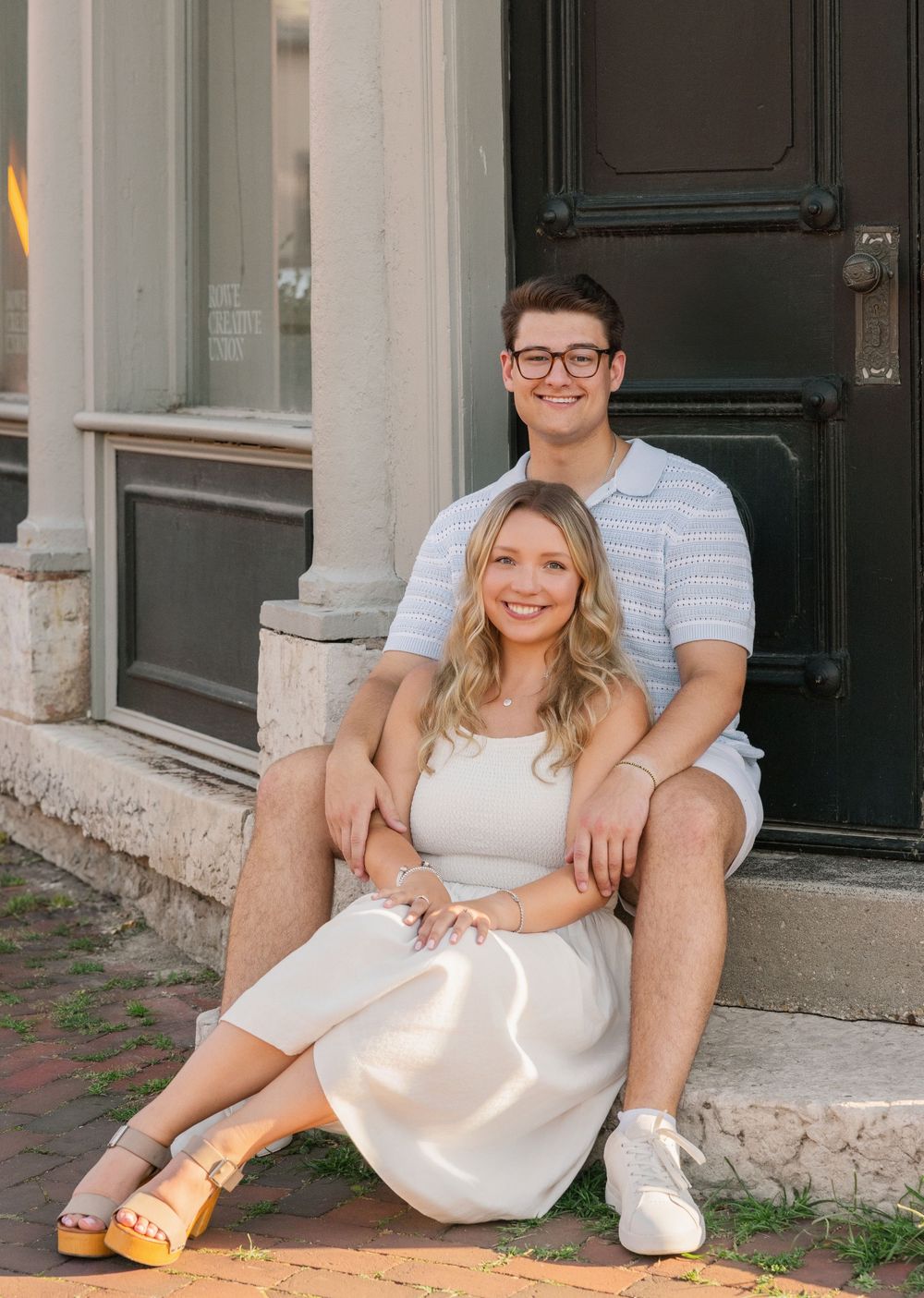 A couple sits together on stone steps outside a building entrance. Mohawk Street German village Engagement.