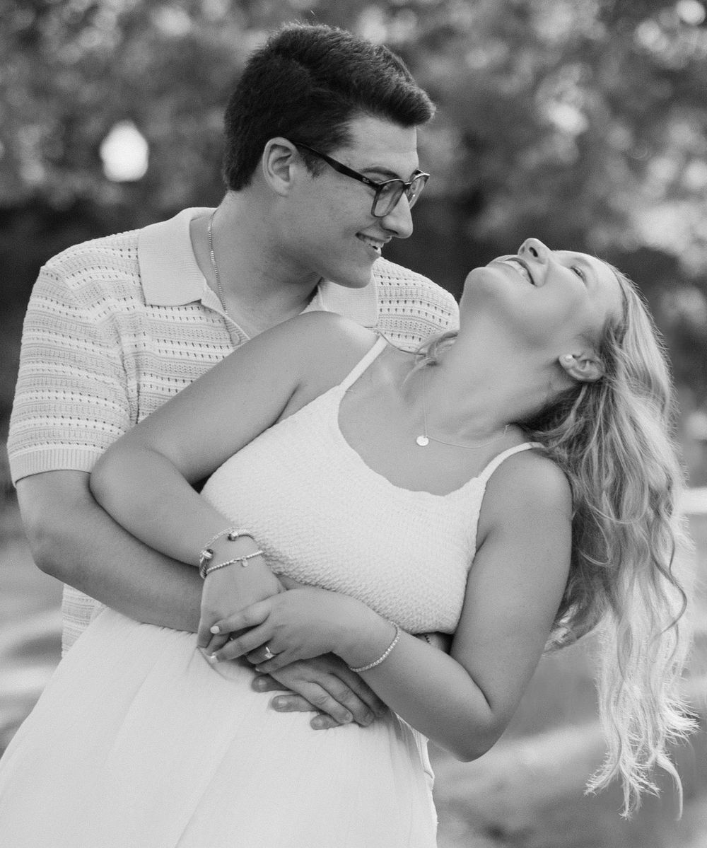 A couple in white outfits embraces romantically in a black and white outdoor photo series. Schiller Park Engagement Session Columbus Ohio.