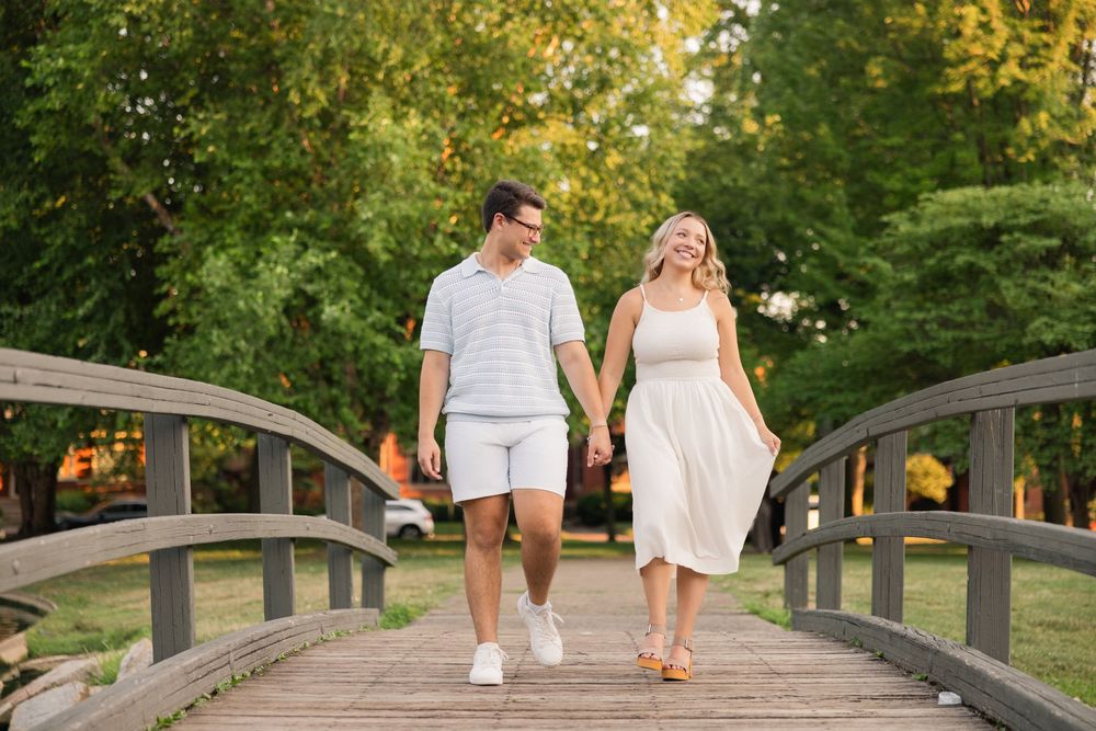 A couple walks across a wooden bridge in a park setting during summer. German Village Columbus Ohio Engagement Session