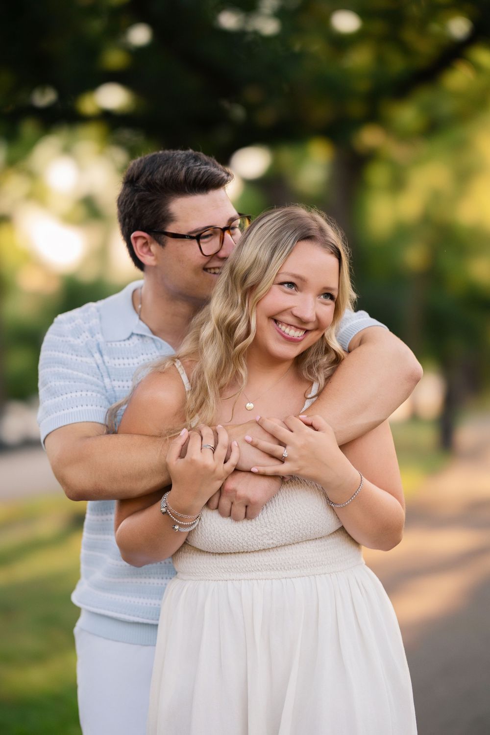 A romantic couple embraces and laughs together in a sunlit park setting during a summer photoshoot. Schiller Park Engagement Session