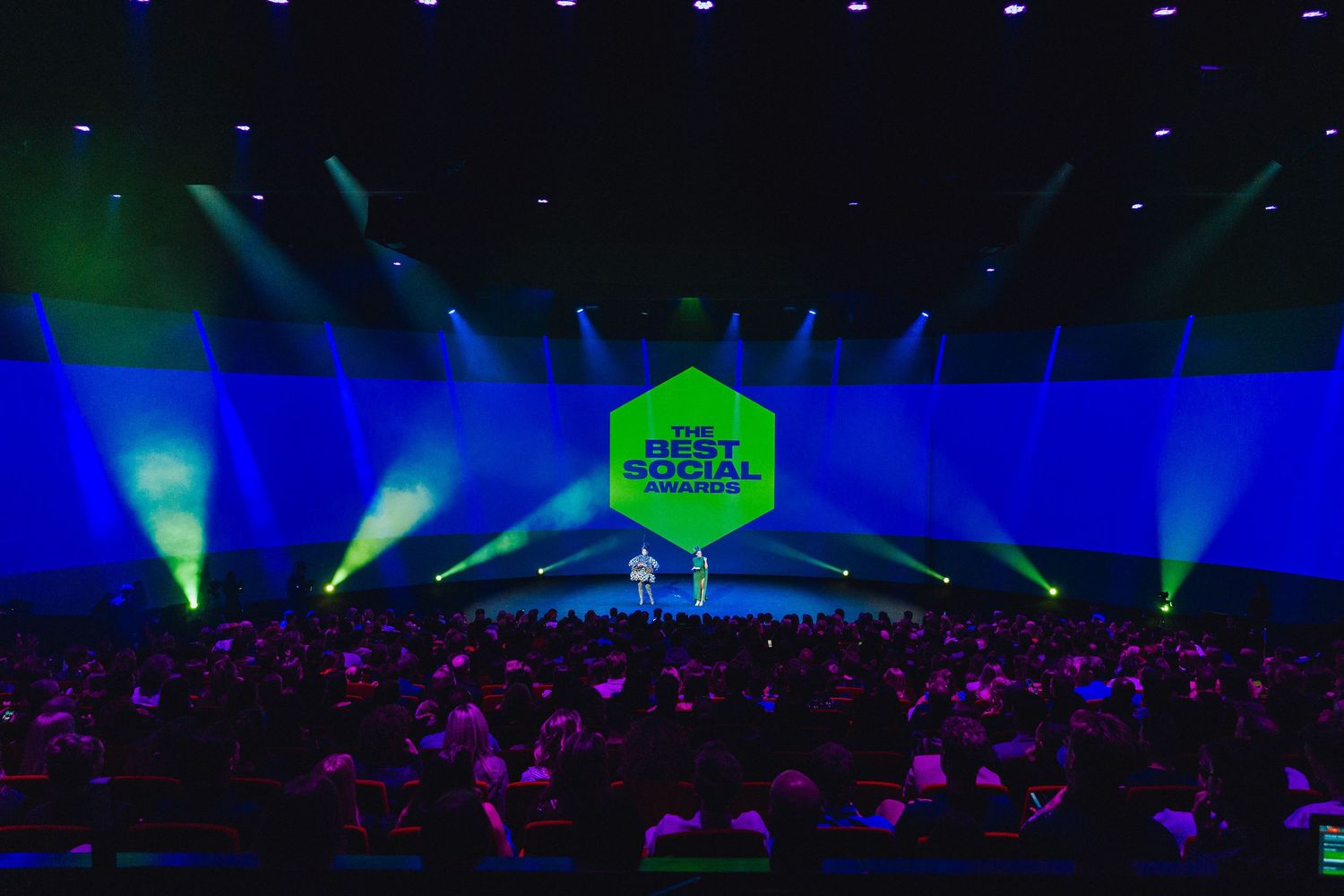 Concert venue with colorful blue and green lighting effects illuminating a large crowd during a live performance.