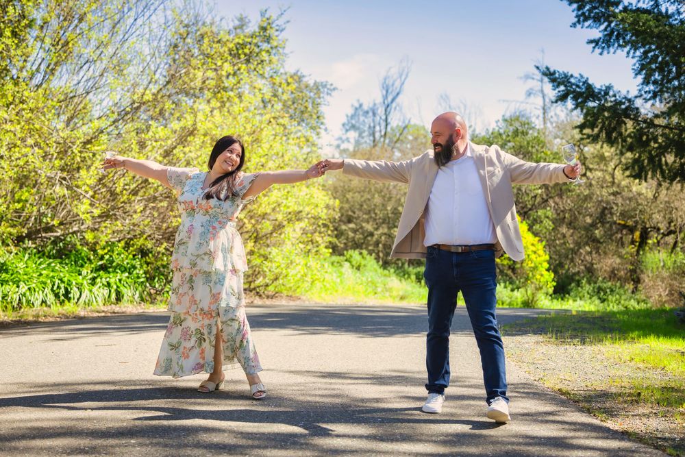 Couple dancing and twirling together on a sunlit path surrounded by green trees and nature.