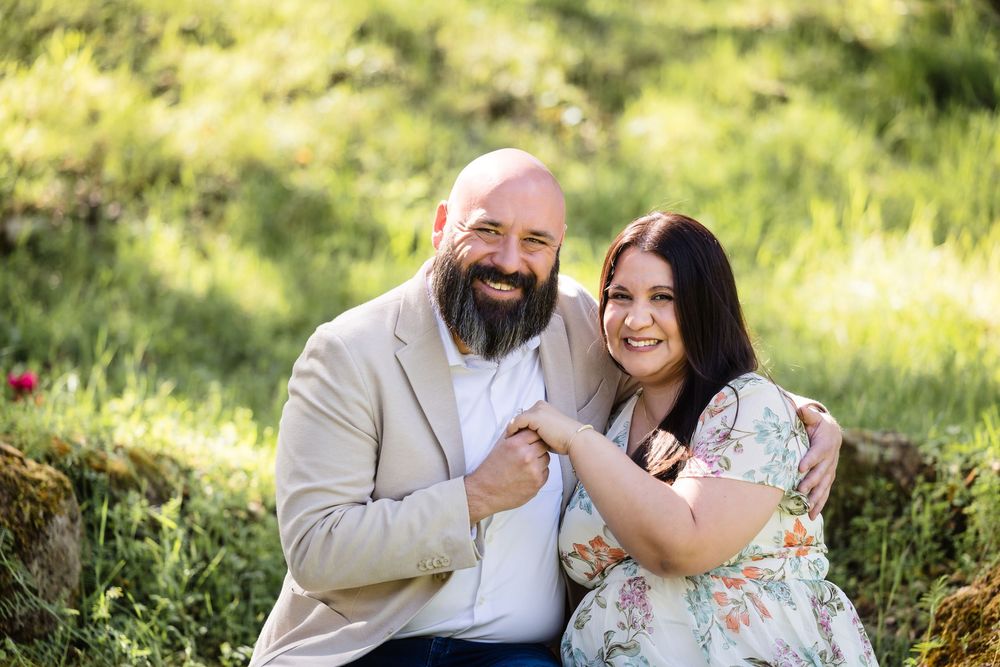 A couple shares a joyful moment together in a sunny outdoor setting with lush greenery in the background.