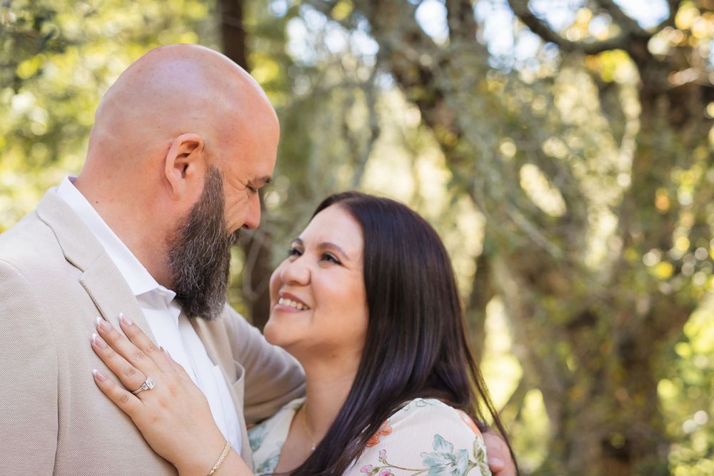 A romantic couple embraces in a sun-dappled forest setting during an outdoor photoshoot.
