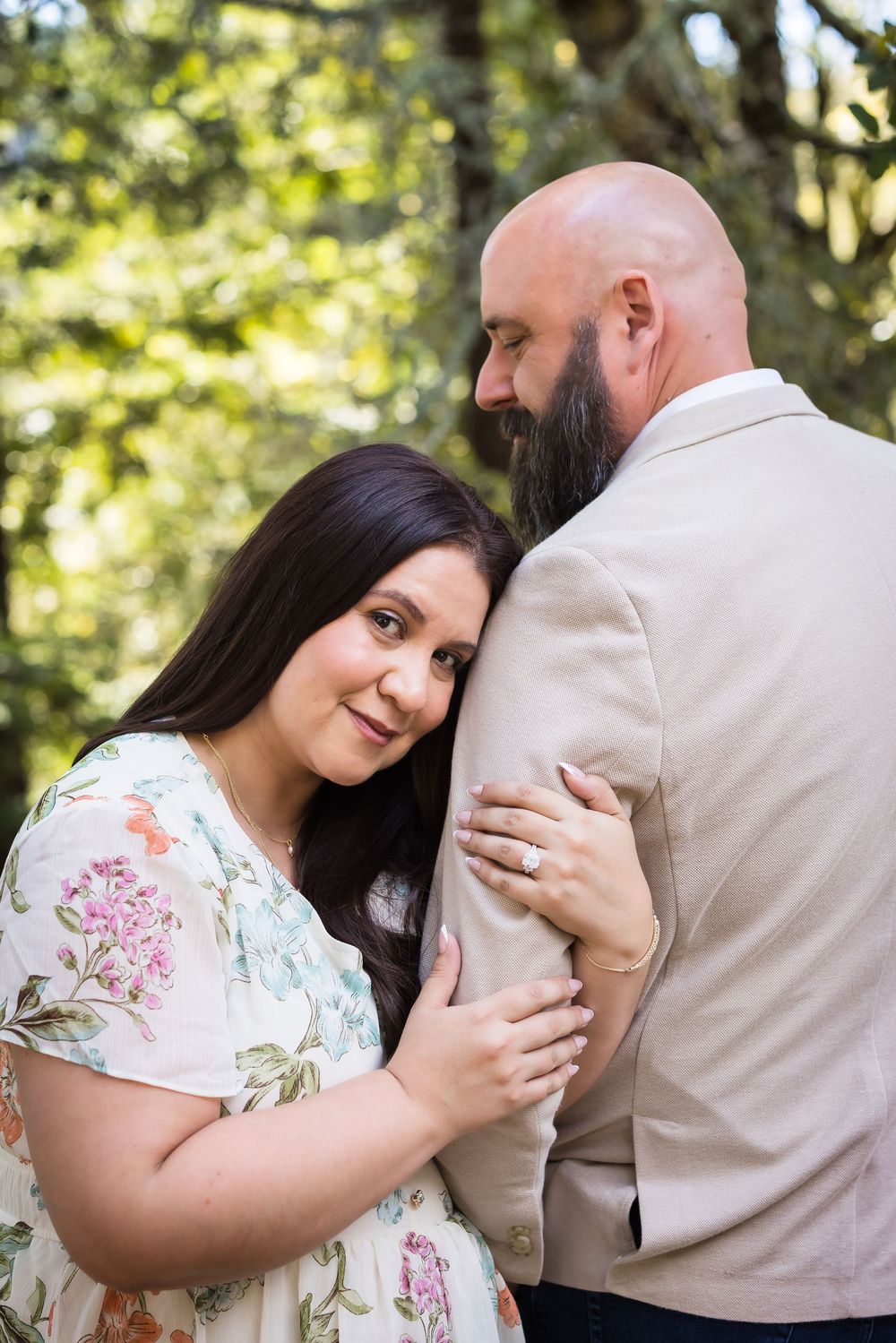 Romantic couple embracing on a wooded path with sunlight filtering through the trees in spring.