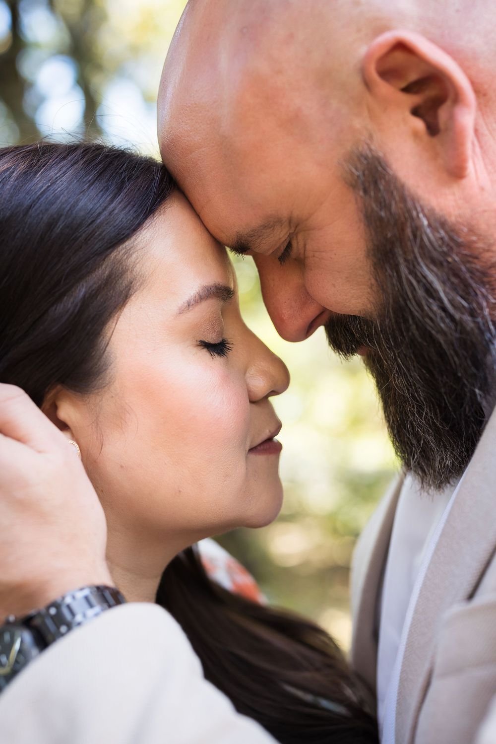 Close up romantic portrait of a couple with foreheads touching in tender embrace outdoors.