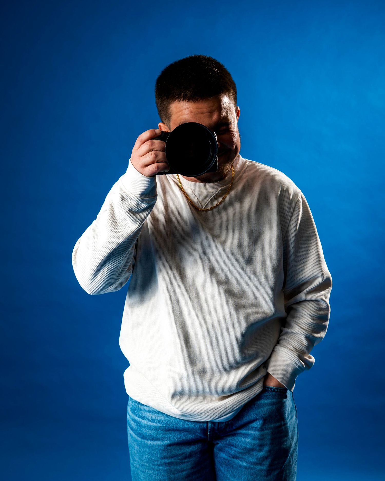 Photographer in white sweater taking photo with camera against blue background.