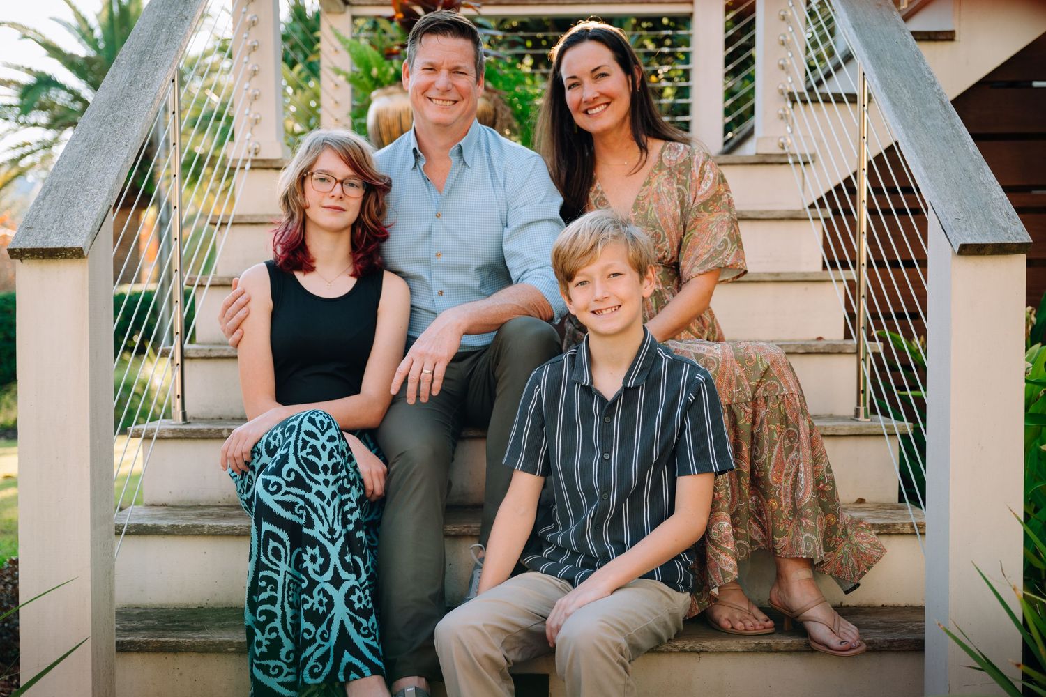 A group of people stand together outdoors in casual attire during a sunny day in a garden setting.
