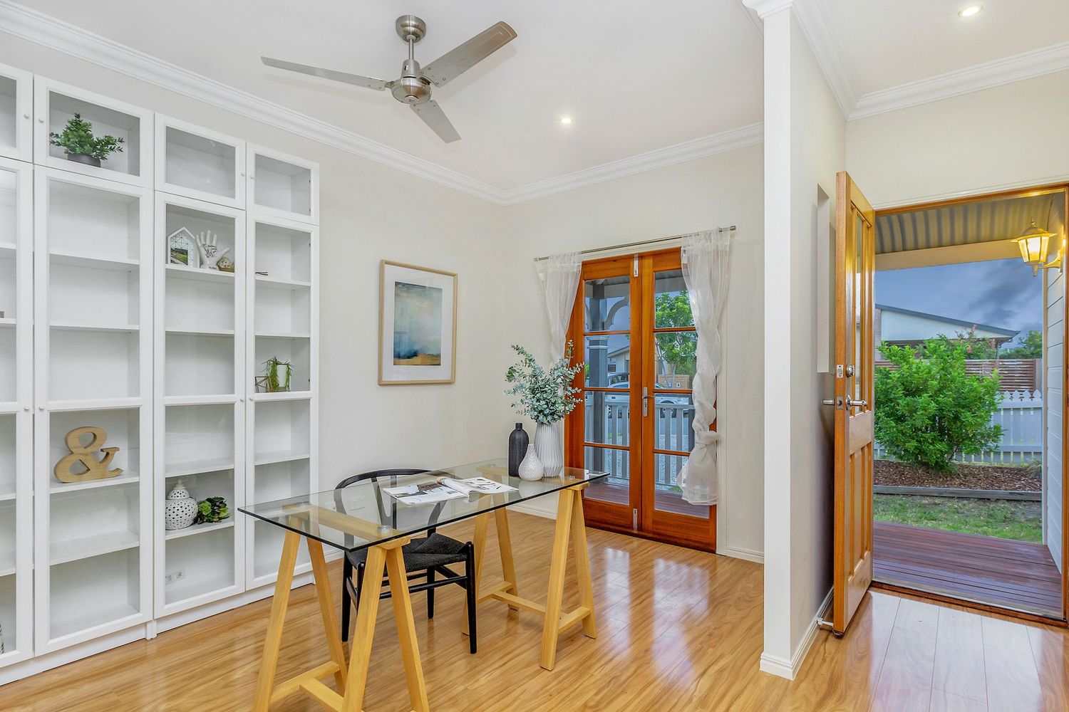 Bright home office with built-in white shelving, timber floors, and French doors.