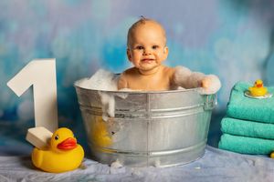 A baby takes a bath in a metal tub with a yellow rubber duck toy and turquoise towels in the background.