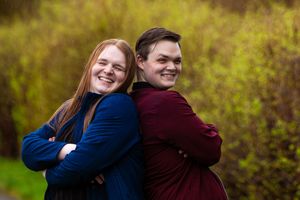A couple embraces and laughs together in an outdoor setting with green foliage in the background.