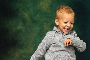A small child in a gray sweater laughs joyfully against a dark green background.