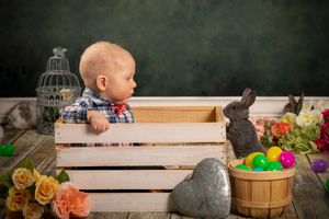 A rustic Easter display with wooden crates, colorful eggs, spring flowers, and a decorative bunny against a dark background.
