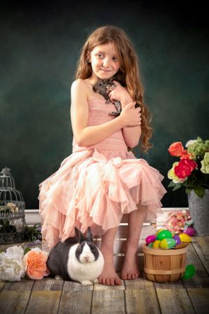 A little girl in a peach dress holding a baby bunny.