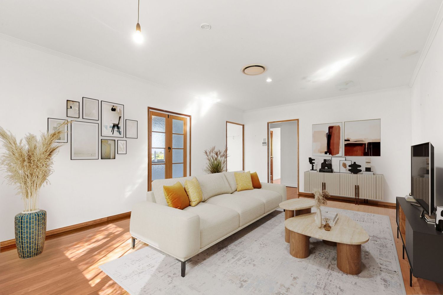 Sunlit living room with beige sofa, timber floors, French doors, and contemporary coastal decor.