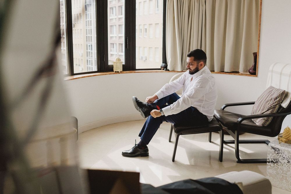 Groom putting on his shoes by the window during wedding preparations in Lisbon.