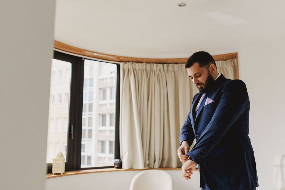 Groom adjusting his blue suit during wedding morning preparations.
