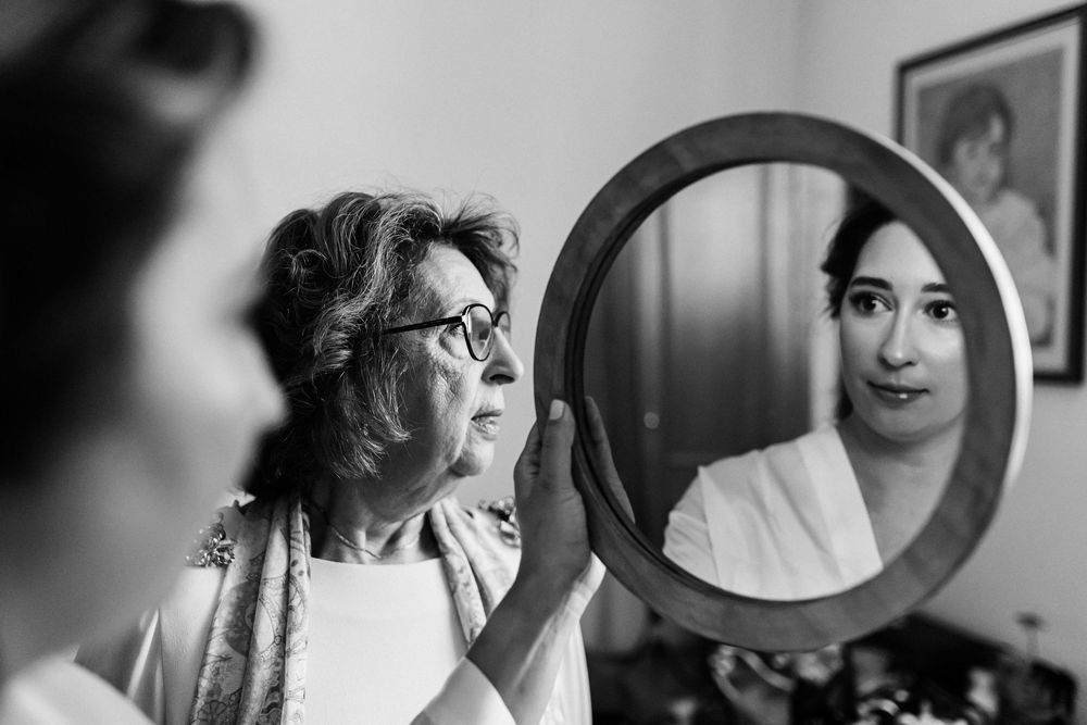 Mother holding a mirror while the bride looks at her reflection during emotional wedding morning preparations.
