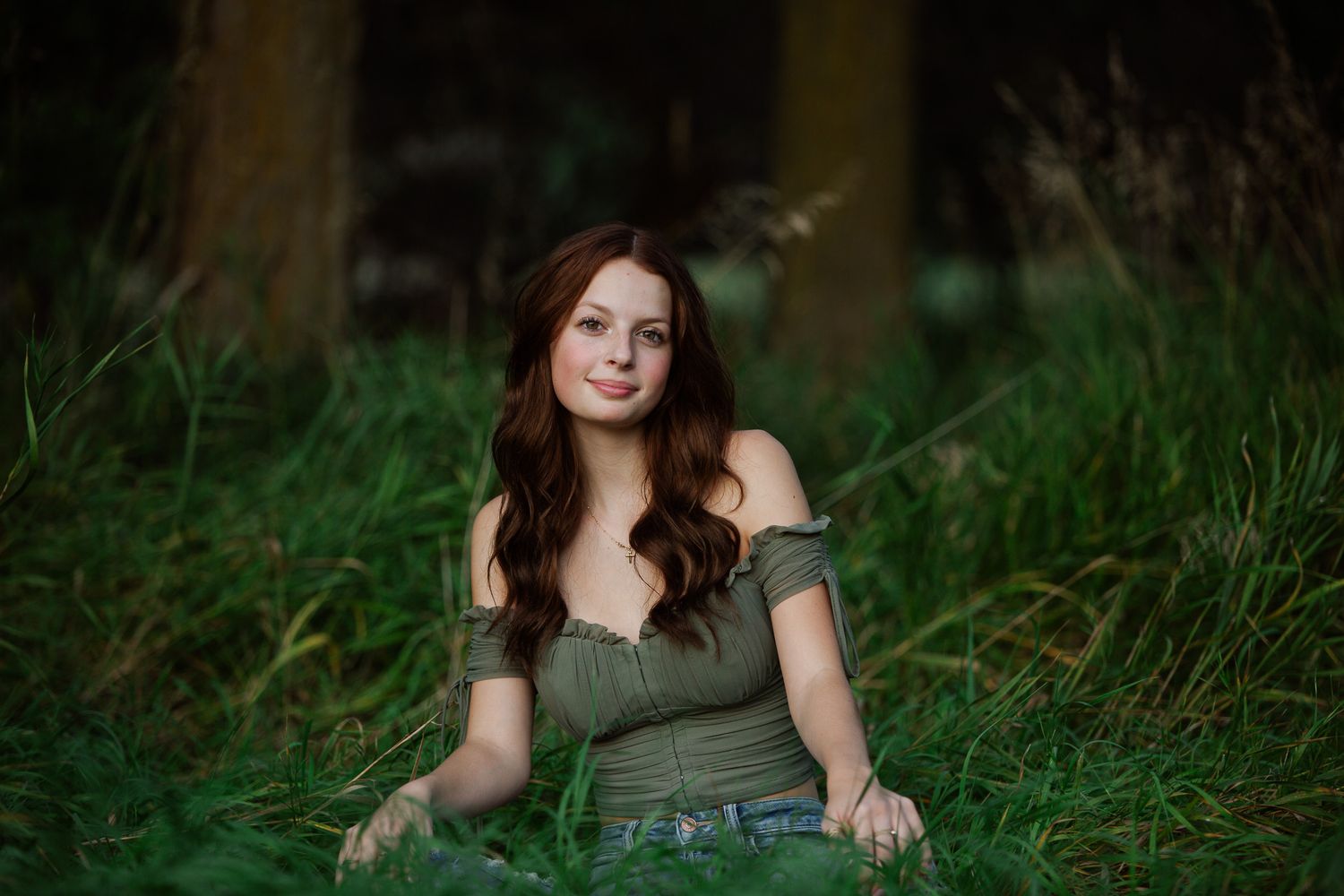 A woman in a green top poses in tall grass during a golden hour outdoor photo session.