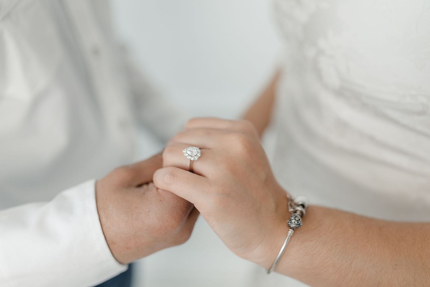 Two hands exchanging a silver engagement ring with a diamond solitaire on a white background.