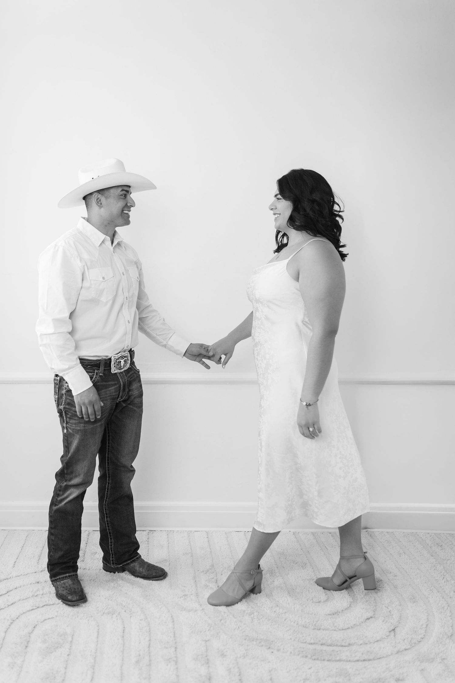 A romantic black and white photo of a couple in western attire sharing a tender moment against a plain wall.