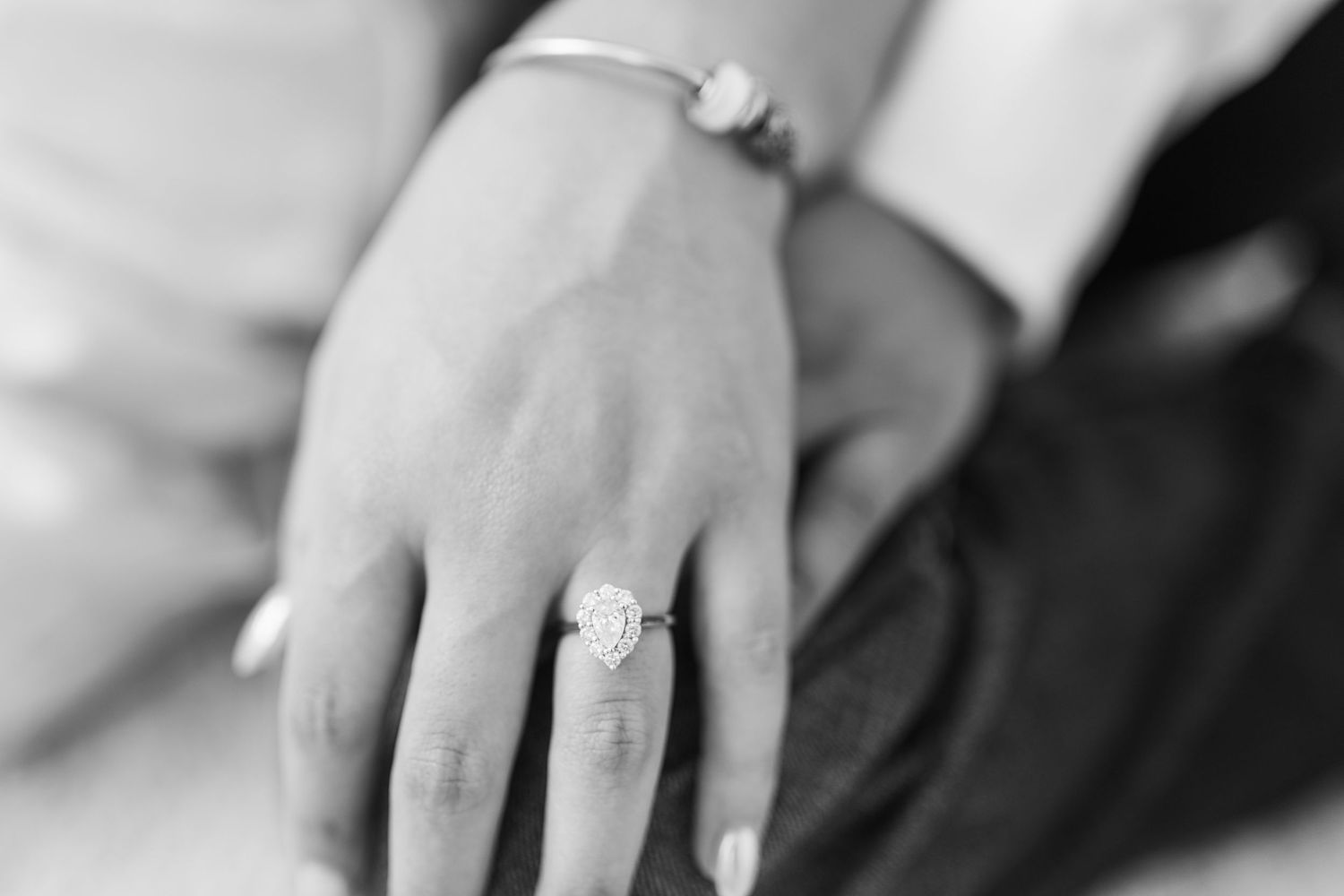 Black and white close-up photograph of a hand wearing an elegant diamond engagement ring.