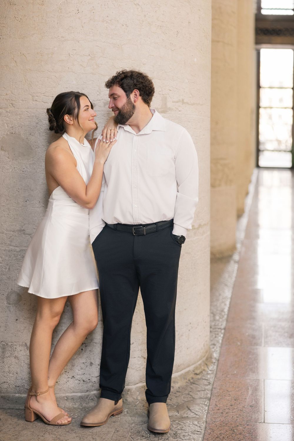A couple in contrasting white and navy outfits shares an intimate moment against a light-colored wall.