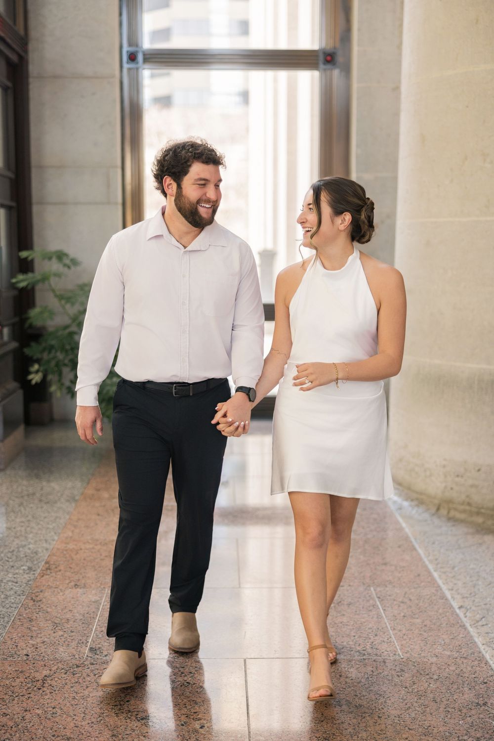 A couple walks together through a bright hallway with polished floors and stone walls.