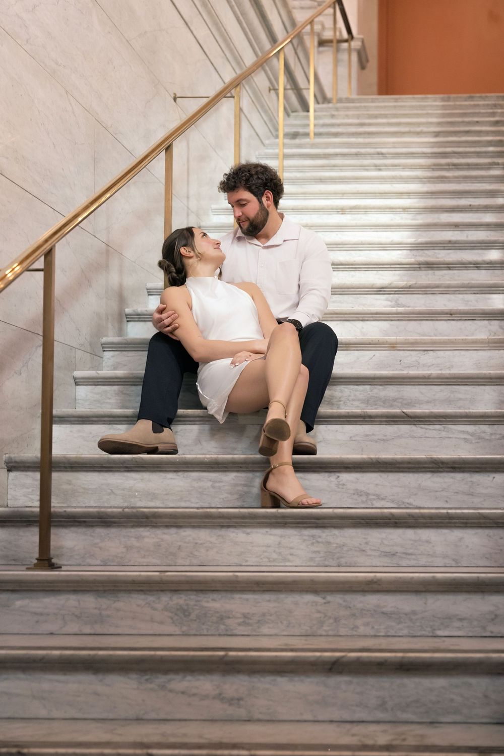 A couple shares an intimate moment while sitting on marble stairs in a romantic engagement photoshoot sequence.