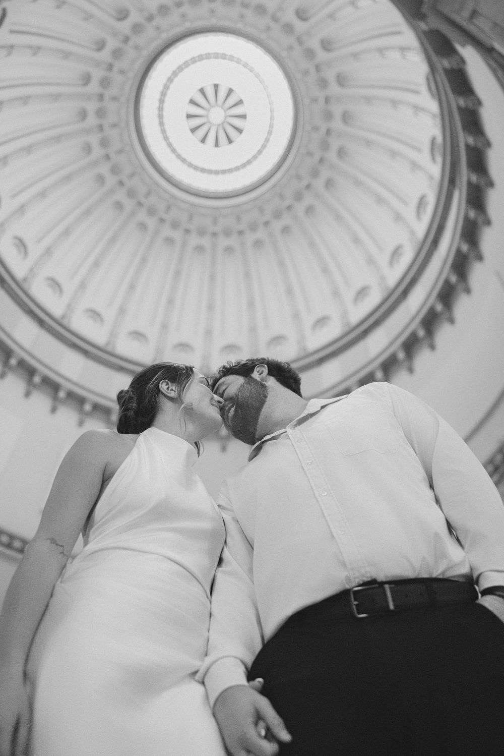 A couple embraces under an ornate domed ceiling with intricate architectural details in black and white. ohio state house