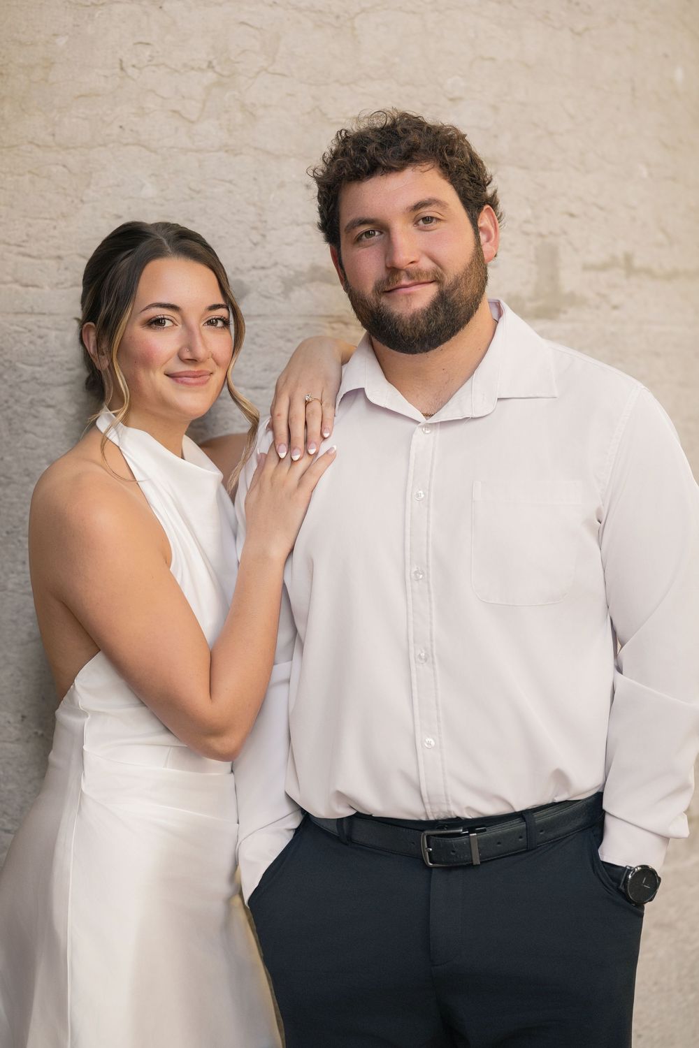 A couple poses together against a neutral wall wearing coordinated white and navy outfits.