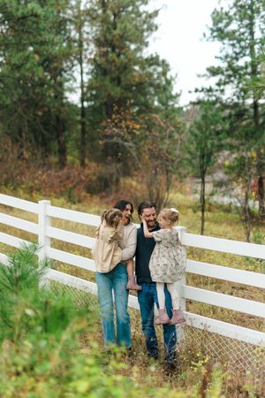 A group stands together by a white wooden fence surrounded by evergreen trees and autumn foliage.