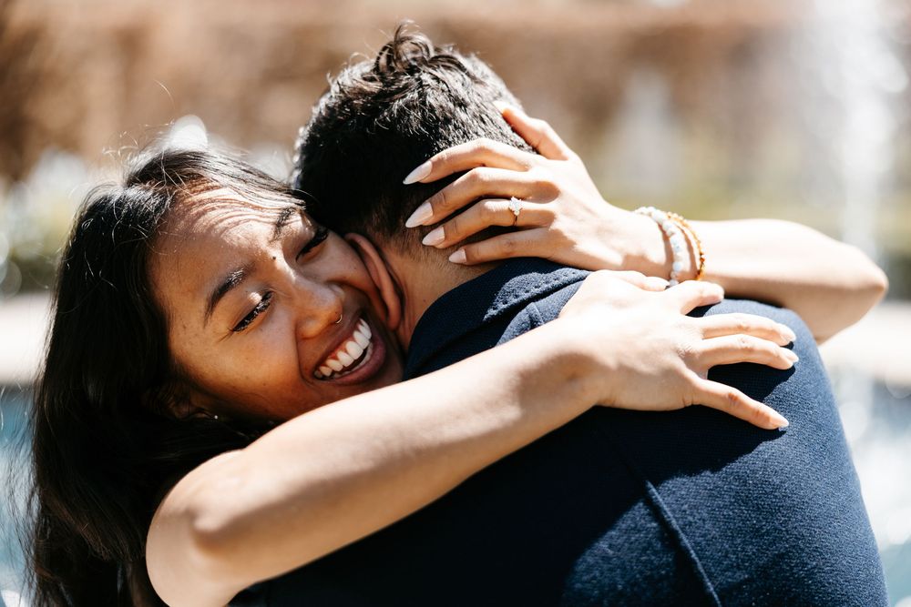 A joyful couple embrace outdoors in warm sunlight while sharing a candid intimate moment together.