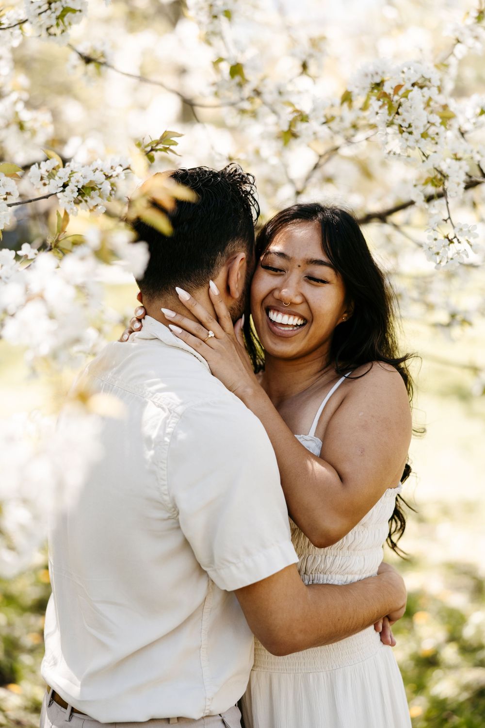 A loving couple embraces under blooming white spring cherry blossoms in a romantic outdoor setting.