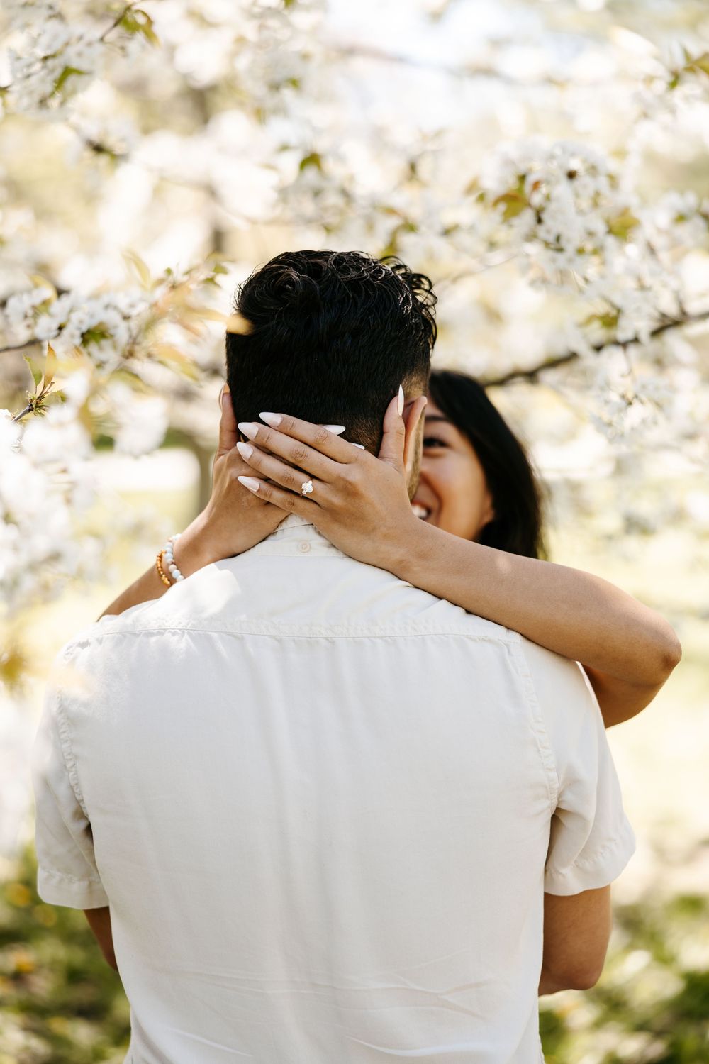A romantic embrace captured under blooming white cherry blossoms on a bright spring day.