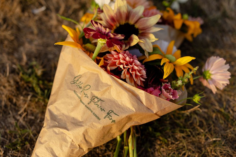 A bouquet of fresh colorful flowers wrapped in brown paper lies on a dark ground in natural lighting.