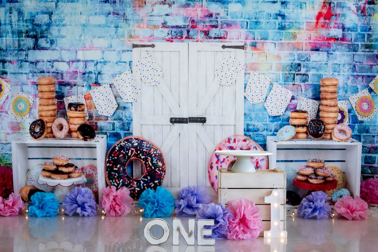 Colourful cake smash photo setup with white backdrop, pink and blue decorations, and confetti for first birthday celebration.